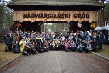 Grupa kilkuset osób w strojach harcerskich na tle drewnianej bramy wjazdowej z napisem: Nadwarciański Gród.