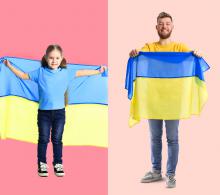 Dziewczynka i mężczyzna trzymają w rękach ukraińską flagę (płótno z dwoma poziomymi pasami: niebieskim i żółtym)