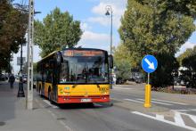 Ulica, po której jedzie czerwono-pomarańczowy autobus komunikacji miejskiej. Nad jego przednią szybą wyświetla się napis: 200 Konstancin-Jeziorna.