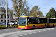 Ulica, po której jedzie czerwono-pomarańczowy autobus komunikacji miejskiej. Nad jego przednią szybą wyświetla się napis: 710 Konstancin-Jeziorna.