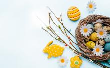 Grafika wektorowa: koszyczek wiklinowy z kolorowymi jajkami. Obok leżą bazie oraz zajączek z ciasta.