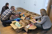 Trzy osoby pakują do kartonowych pudełek artykuły spożywcze i higieniczne. 