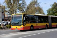 Ulica, po której jedzie czerwono-pomarańczowy autobus komunikacji miejskiej. Nad jego przednią szybą wyświetla się napis: 710 Konstancin-Jeziorna.