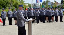 Funkcjonariusze policji w umundurowaniu stoją na baczność w rzędzie. Przed nimi mężczyzna w umundurowaniu przemawia do mikrofonu.