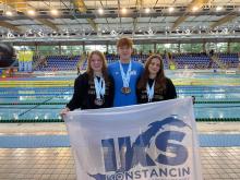 Trzy osoby na tle basenu trzymają flagę z logo IKS Konstancin.
