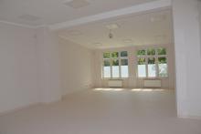 Zdjęcie pomieszczenia, sali pomalowanej na biało. W dali widać duże przeszklone okna. 