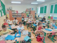 dzieci siedzące w klasie w szkolnych ławkach