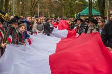 Grupa osób trzyma długą biało-czerwoną flagę.