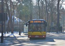 Ulica, po której jedzie czerwono-pomarańczowy autobus komunikacji miejskiej. Nad jego przednią szybą wyświetla się napis: 200. 