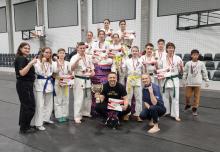 Młode dziewczyny i chłopcy w strojack zawodników karate. Na szyjach mają zawieszone medale, a w dłoniach dyplomy. Przed nimi kuca męzczyzna z pucharem w dłoni i kobieta.