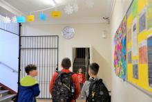 Szkolny korytarz, trzech uczniów patrzy w górę na zegar zawieszony na ścianie. 
