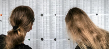 Dwie dziewczynki patrzą ta tablice, na której wywieszone jest wyniki egzaminów. 