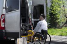 Mężczyzna na wózku inwalidzkim przy otwartych tylnych drzwiach do samochodu.