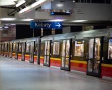 Wagony metra stoją przy peronie. W środku siedzą ludzie, a nad peronem jest tabliczka z napisem: Kabaty.