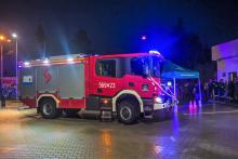 Duży wóz strażacki w kolorze czerwonym i metalicznym stoi zaprakowany na wybrukowanym placu. 