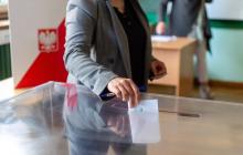 Lokal wyborczy, kobieta wrzuca kartkę do urny wyborczej