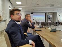 Mężczyzna w garniturze i w okularach siedzi za stołem w sali konferencyjnej