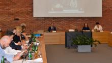 Grupa osób siedzi przy stołach w sali posiedzeń.