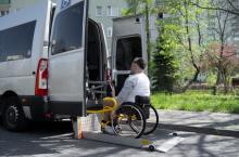 Osoba na wózku inwalidzkim, przed samochodem transportowym 