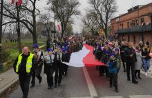Grupa osób niesie biało-czerwoną flagę.