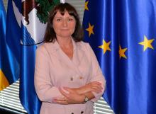 Kobieta z założonymi rękoma na tle flag Konstancina-Jeziorny i Unii Europejskiej.