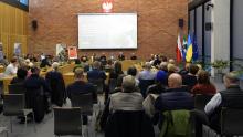 Sala posiedzeń wypełniona osobami siedzącymi na krzesełkach