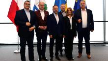 Grupa osób ubrana w garnitury na tle flag.