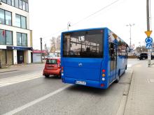 Niebieski autobus stoi na przystanku, w tle ulica z samochodami.