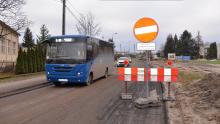 Niebieski autobus komunikacji miejskiej przejeżdżający przez drogę w trakcie remontu, oznaczoną zakazem wjazdu z wyłączeniem pojazdów budowy i mieszkańców. Po prawej stronie widać barierki oraz oznaczenia ostrzegawcze, a w tle maszyny budowlane i sprzęt wykorzystywany podczas prac.