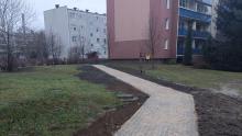 Nowo wyłożony chodnik z kostki brukowej otoczony terenem zielonym i blokami mieszkalnymi w zimowej scenerii.