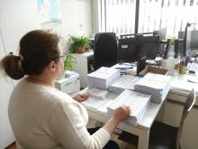 Kobieta siedzi przy biurku i pakuje listy do koperty. 
