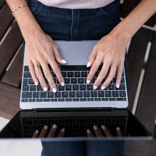 Kobieta z pomalowanymi na biało paznokciami pracuje na laptopie, trzymając dłonie na klawiaturze.