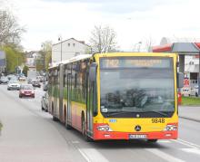 Przegubowy autobus Mercedes-Benz w żółto-czerwonych barwach warszawskiej komunikacji miejskiej, kursujący na linii 742 do Góry Kalwarii, jadący po miejskiej drodze wśród innych pojazdów.