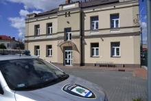 Piętrowy budynek straży miejskiej, na pierwszym planie fragment samochodu z herbem gminy na masce.