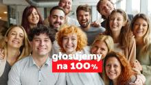 Grupa uśmiechniętych ludzi pozuje razem do zdjęcia, a na pierwszym planie widnieje hasło „głosujemy na 100%” na czerwono-białym tle.