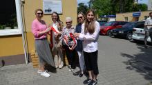 Pięć kobiet, w tym uczennica i seniorka, trzyma wstęgę podczas uroczystego odsłonięcia tablicy pamiątkowej na budynku przy ul. Jana Sobieskiego 6 w Konstancinie-Jeziornie.