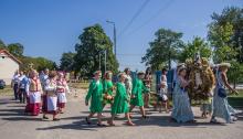 Kolorowy korowód dożynkowy z udziałem mieszkańców w tradycyjnych strojach ludowych i dziewcząt niosących wieniec z kłosów zbóż podczas święta plonów.