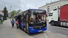 Niebieski autobus stoi na przystanku, w tle ulica z samochodami.