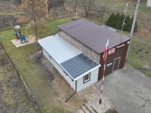 Widok z lotu ptaka na budynek Ochotniczej Straży Pożarnej w Słomczynie z placem zabaw w tle i maszt z polską flagą przed wejściem.