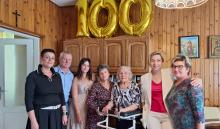 Rodzinne zdjęcie - grupa osób stoi, w środku solenizantka. Nad nimi złoty balon - liczba 100.
