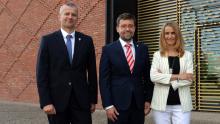 Na zdjęciu trzech uśmiechniętych przedstawicieli samorządu gminy Konstancin-Jeziorna pozuje przed nowoczesnym budynkiem z ceglaną i przeszkloną elewacją.
