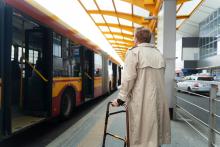 Kobieta stoi na przystanku autobusowym i chce wsiąść do pojazdu.