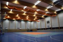 Wnętrze dużej, nowoczesnej hali sportowej z wieloma koszami do koszykówki, niebieską podłogą i pomarańczowymi siatkami pod sufitem.