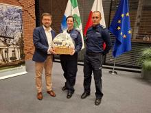 trzy osoby stoją na tle flag trzymając kosz z białymi maskotkami