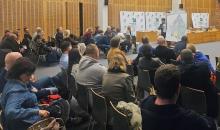 Grupa ludzi siedzi na krzesłach w sali konferencyjnej i słuch prezentacji.