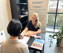 Dwie kobiety siedzą naprzeciwko siebie. Jedna z nich pokazuje drugiej dokument.