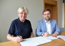 Dwóch mężczyzn siedzi przy stole i podpisuje dokumenty podczas zawarcia porozumienia dotyczącego współpracy Muzeum Villa la Fleur z Konstancińską Kartą Mieszkańca.