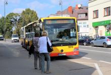 Żółto-czerwony autobus linii 710 zatrzymuje się na przystanku w centrum Konstancina-Jeziorny, gdzie na chodniku czekają pasażerowie.