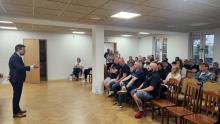 Grupa osób w sali świetlicowej słucha wystąpienia burmistrza