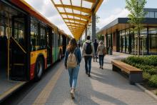 Wizualizacja nowoczesnego węzła przesiadkowego z autobusem, budynkiem poczekalni oraz pasażerami korzystającymi z infrastruktury transportu publicznego.